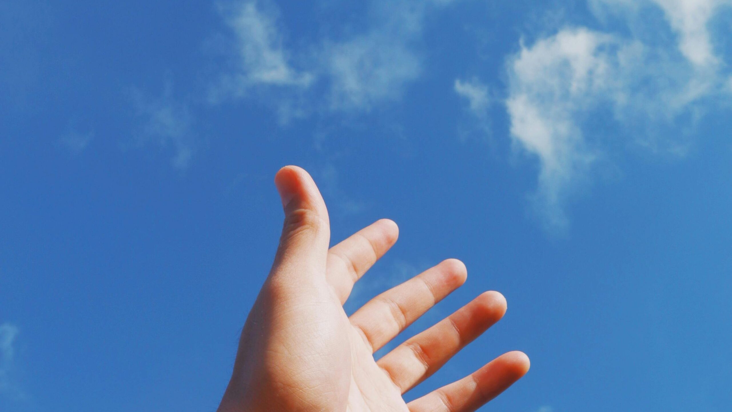 Light-skinned human hand reaching up to a blue sky